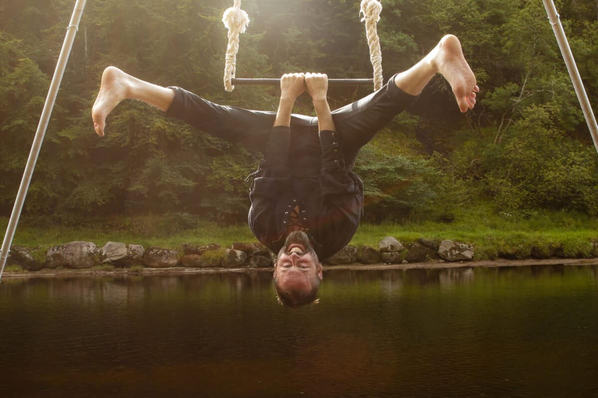 Ruaraidh smiling in straddle on trapeze over river. Photo: Daniel Lacasta Fitzsimmons